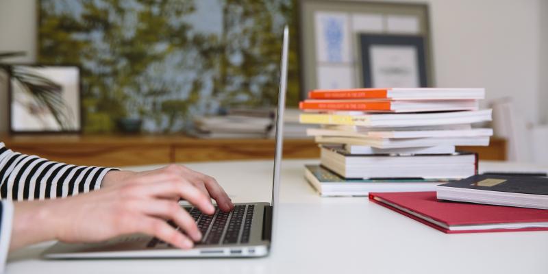 A person uses a computer. Stack of books in the background.