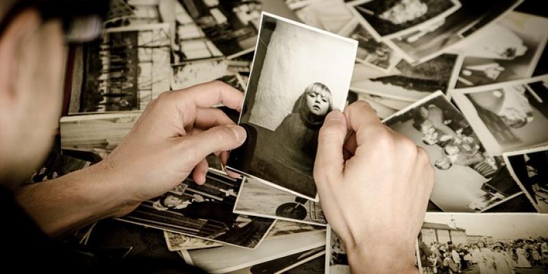 Kuvituskuva: Taustalla lukuisia mustavalkoisia valokuvia. Etualalla ihminen, jonka käsissä on mustavalkoinen valokuva tytöstä. 