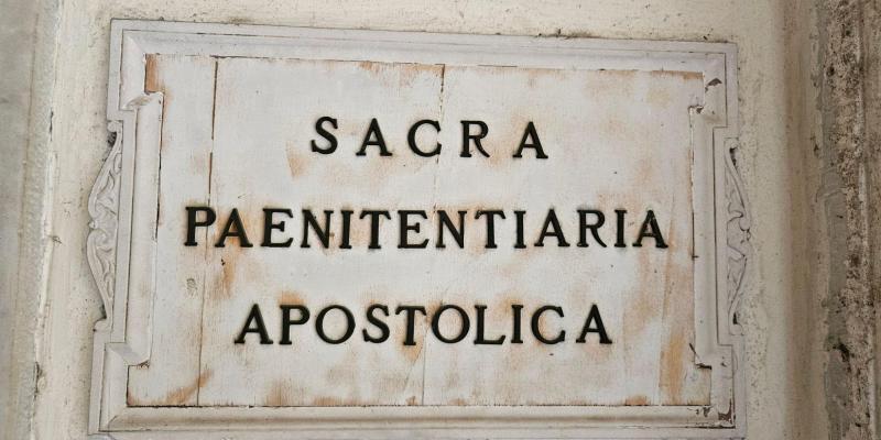 Kuvassa näkyy lähikuvassa Palazzo della Cancellerian seinällä oleva valkotaustainen kivinen kyltti, jossa on metallisin kirjaimin suuraakkosin kirjoitettu: SACRA PAENITENTIARIA APOSTOLICA.