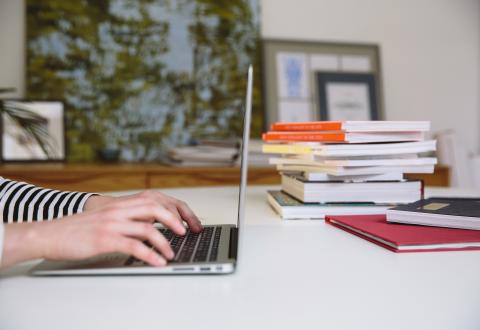 A person uses a computer. Stack of books in the background.